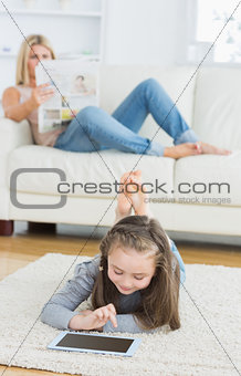 Girl using tablet and mother reading newspaper