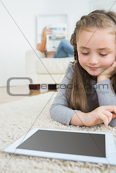 Girl using tablet with her mother reading the newspaper on the couch