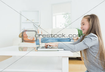 Girl working on laptop with her mother reading the newspaper