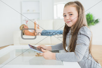 Little girl using tablet while mother is reading newspaper