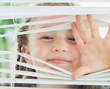 Smiling girl looking through the blinds