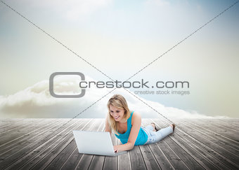 Cute blonde woman laying and using laptop over wooden boards