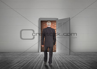Businessman walking towards door open but blocked by red brick wall