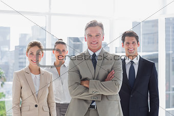 Boss with his arms folded standing with smiling colleagues behind