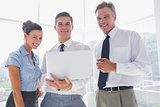 Three smiling business people holding a laptop