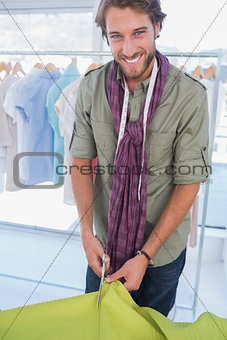 Smiling fashion designer cutting textile