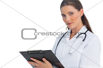 Serious nurse writing on clipboard and looking at camera