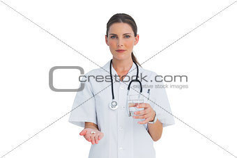 Serious nurse holding medicine and glass of water