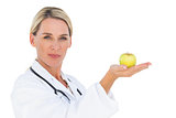 Happy doctor holding out green apple and looking at camera