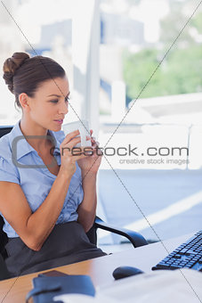 Businesswoman holding her mug and looking at her computer
