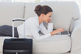 Business woman lying on couch with laptop and suitcase