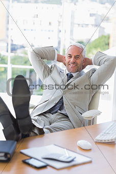 Businessman relaxing at his desk and smiling at camera