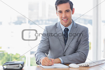 Smiling businessman writing at his desk
