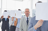 Business team covering face with white paper except for one