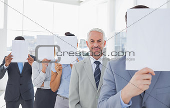 Business team covering face with white paper except for one