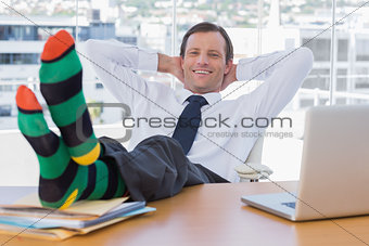 Smiling businessman relaxing with feet on his desk