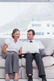 Businessman and woman sitting on couch and using laptop
