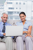 Business people with laptop smiling at camera sitting on couch