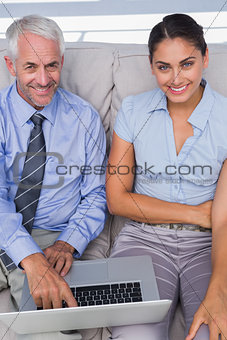 Business people using laptop on the couch and smiling up at camera