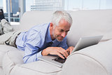 Businessman lying on couch using laptop
