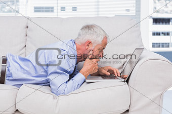 Businessman lying on sofa with laptop