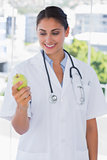Happy young doctor holding a green apple
