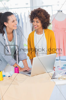 Two cheerful fashion designers working on a laptop