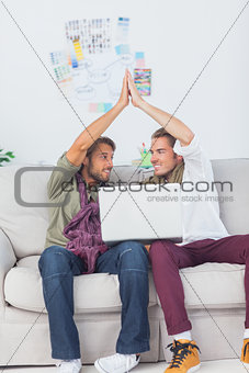 Designers working together with a laptop then high fiving