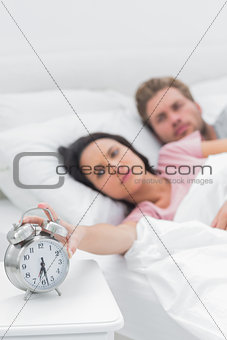 Tired woman turning off the alarm clock