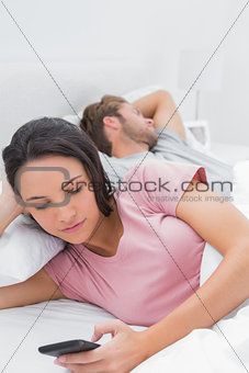 Woman using her phone while her partner is sleeping