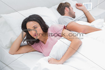 Woman thinking in her bed next to her sleeping husband