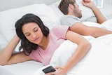 Woman using her phone while her husband is sleeping