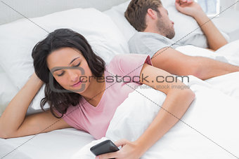 Woman using her phone while her husband is sleeping