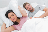 Woman covering her ears with pillow while her husband is snoring