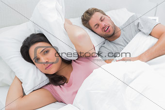 Woman covering ears with pillow while her husband is snoring