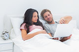 Couple lying in bed looking at a laptop