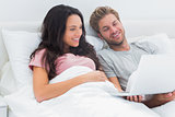 Couple in bed looking at their laptop