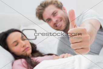 Man giving thumb up while his wife is sleeping
