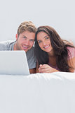 Cheerful couple using a laptop in bed