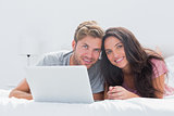 Cheerful couple with laptop in bed