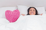 Woman lying in bed next to a fluffy heart pillow
