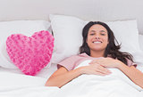 Woman lying in her bed next to a pink heart pillow