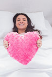 Woman lying in her bed and holding a fluffy heart cushion