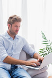 Serious man using his laptop on a couch