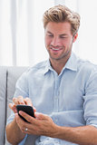 Cheerful man using his smartphone on a couch