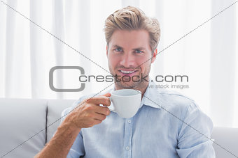 Handsome man sitting on his couch drinking a coffee