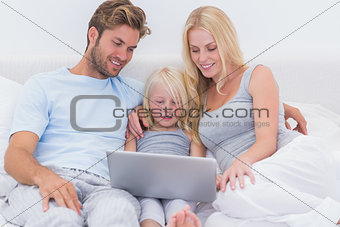 Cheerful family using a laptop in bed