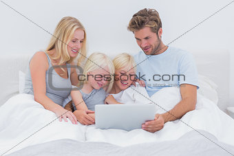 Beautiful family using a laptop in bed