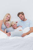 Cheerful family using a laptop in bed