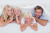 Portrait of a family smiling under quilt